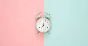 An alarm clock positioned in front of a pink and blue background.