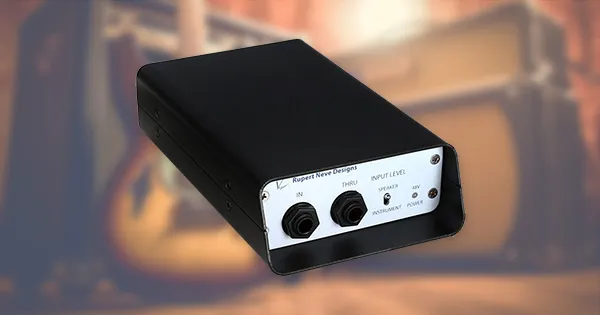 An image of a DI box in front of a guitar and amplifier.