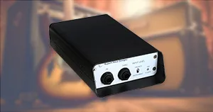 An image of a DI box in front of a guitar and amplifier.